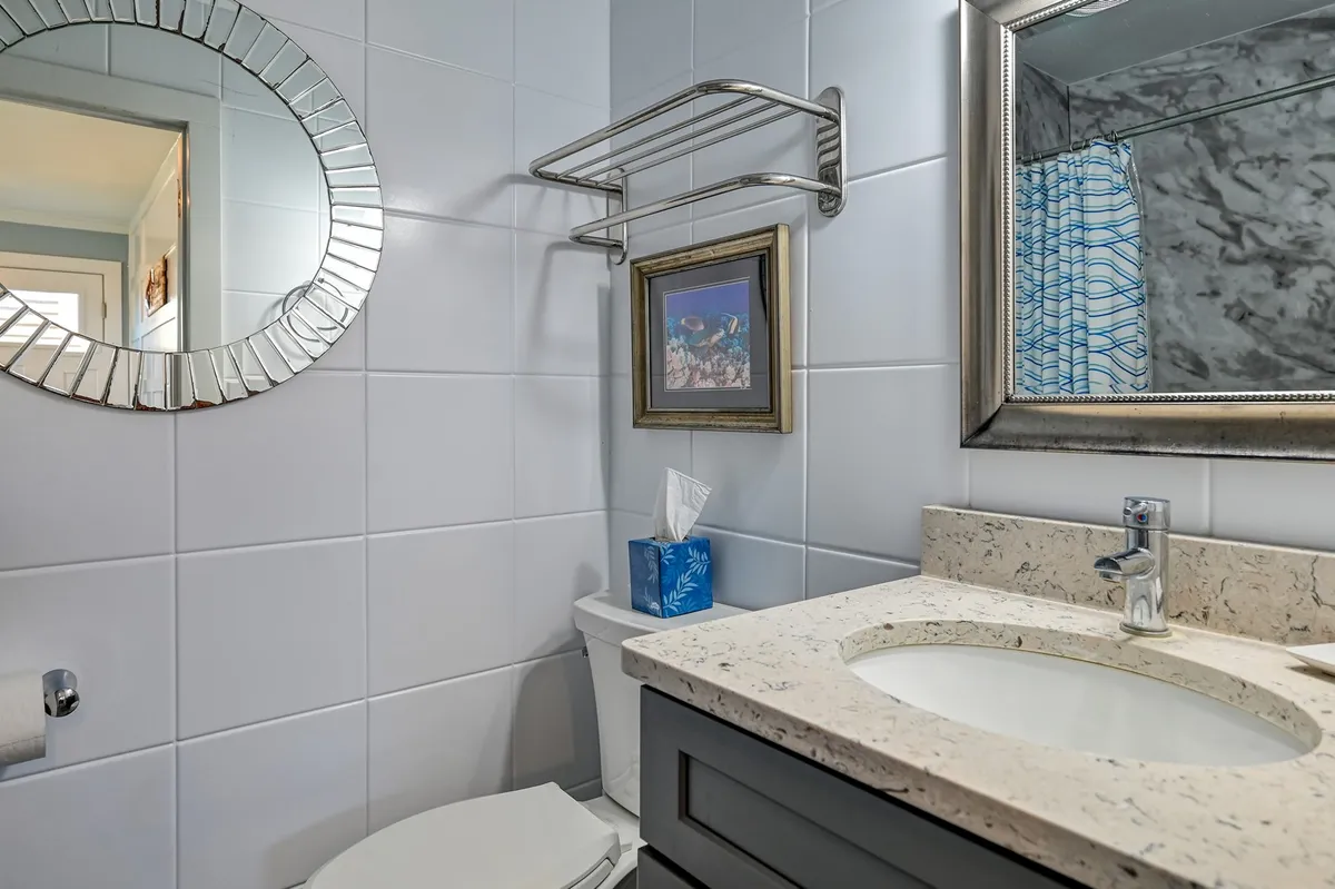 A tidy bathroom with a mirror, framed artwork, sink, and towel rack, designed for easy post-beach clean-up and personal refreshment. The surfaces are practical and easy to clean.