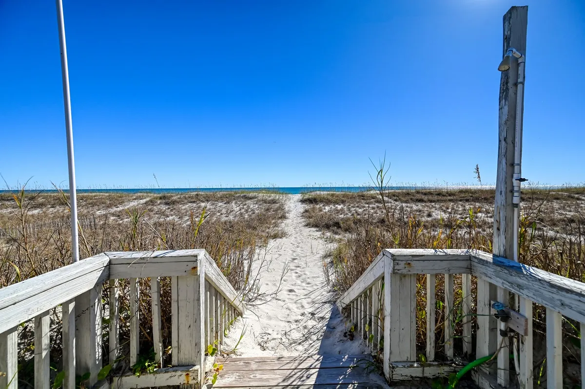 Wooden steps descend from a boardwalk directly onto the sand, opening up to a breathtaking view of the ocean. The scene feels serene and private, with the gentle curves of the dunes and the vast expanse of water in the background. The early morning light suggests a tranquil moment, ideal for sunrise strolls or quiet reflection.