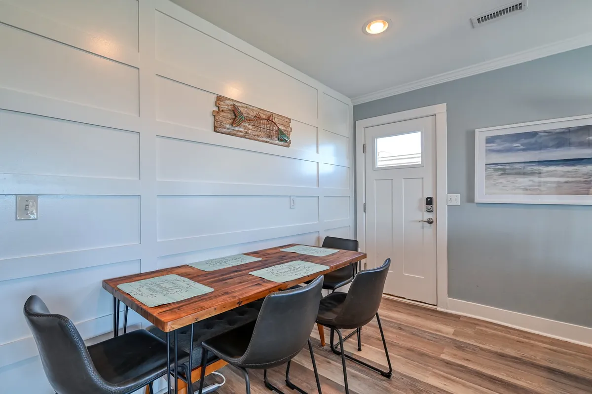 A warm and welcoming dining area featuring a wooden table surrounded by black chairs, adorned with wall art and natural lighting. The setting feels ideal for gathering with friends and family to share stories or plan excursions.