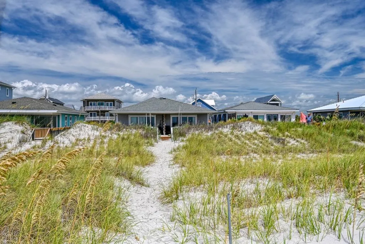 An exterior shot showcasing a soft sand path winding through dune grass, flanked by beach houses. The area is ideal for relaxed beach walks, sunsets, and family fun, reflecting a peaceful yet vibrant beach environment.