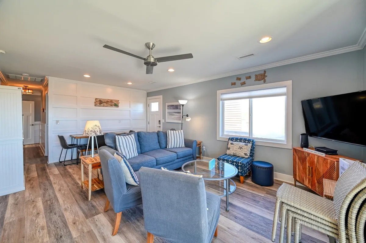 A welcoming living room decorated in blue and white, featuring a striped sofa, glass coffee table, modern TV unit, and nautical wall art. The space is filled with natural light, creating an inviting environment for families to gather after a day of local exploration.