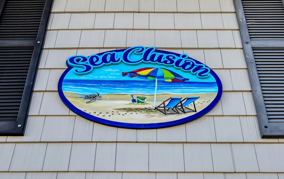 This image captures a cheerful outdoor scene with beach chairs and an umbrella set up on the sand, accompanied by signage that evokes a sense of place. The mood is bright and inviting, suggesting fun family moments spent by the ocean, relaxing, and participating in beach activities.