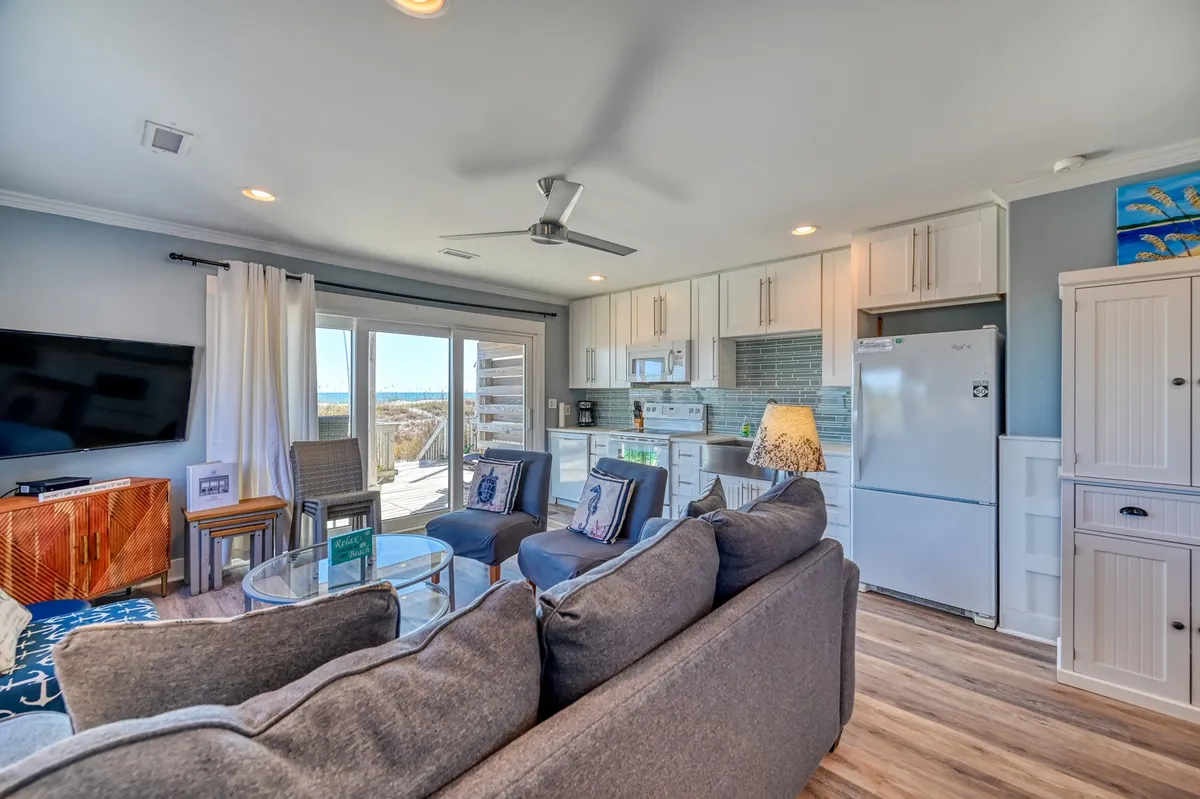 A spacious, open-plan area with a comfortable sofa, coffee table, television, and kitchen, all basked in natural light from windows that hint at exterior views. The layout encourages togetherness, with spaces for relaxing, preparing meals, and watching the sunset.